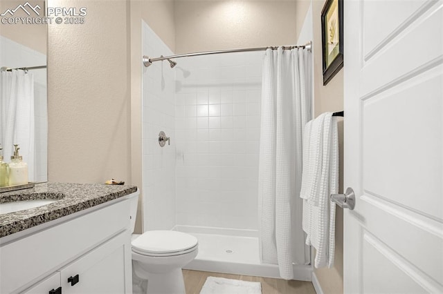 bathroom with toilet, a stall shower, a textured wall, and vanity