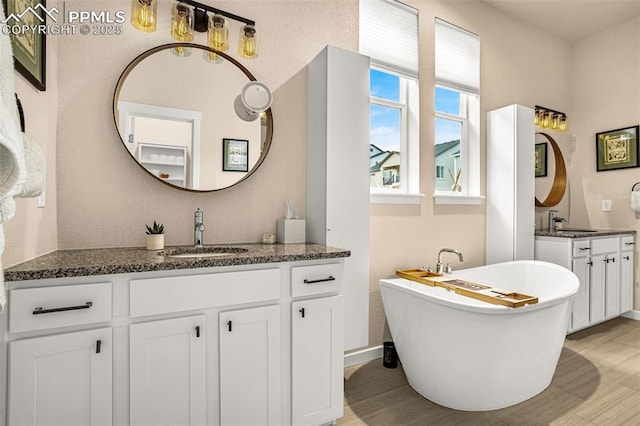 bathroom featuring a soaking tub, two vanities, a sink, and wood finished floors