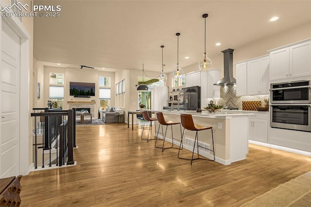 kitchen with a kitchen breakfast bar, light wood-style floors, wall chimney range hood, freestanding refrigerator, and tasteful backsplash