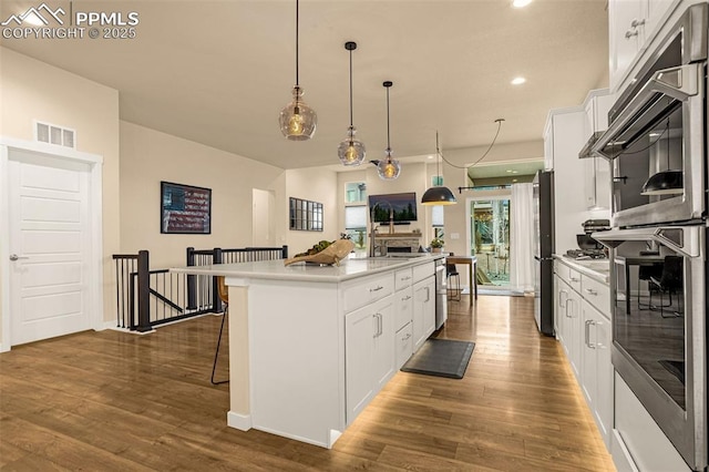 kitchen featuring stainless steel appliances, dark wood-type flooring, a kitchen breakfast bar, white cabinets, and an island with sink