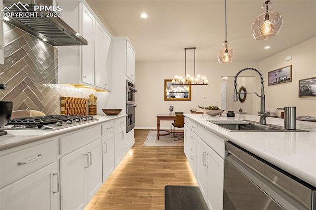 kitchen with a sink, white cabinets, light wood-style floors, wall chimney range hood, and appliances with stainless steel finishes