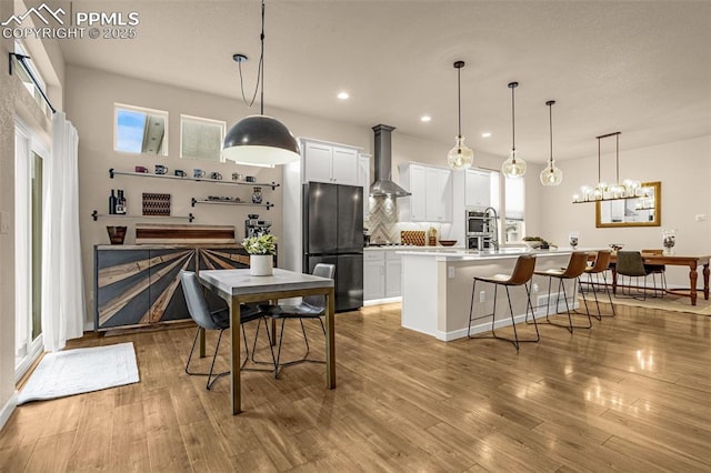 kitchen with wall chimney exhaust hood, a breakfast bar area, light wood-style flooring, and freestanding refrigerator