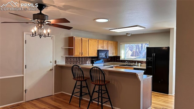 kitchen with black appliances, light wood-style flooring, a sink, backsplash, and a peninsula