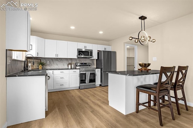 kitchen featuring light wood finished floors, dark countertops, appliances with stainless steel finishes, white cabinetry, and a sink