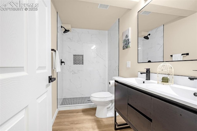 full bath featuring toilet, a tile shower, a sink, and wood finished floors