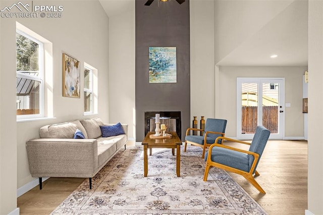 living room with a fireplace, a towering ceiling, baseboards, and wood finished floors