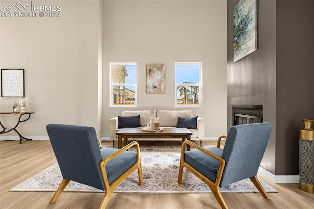 sitting room with a towering ceiling, a large fireplace, baseboards, and wood finished floors