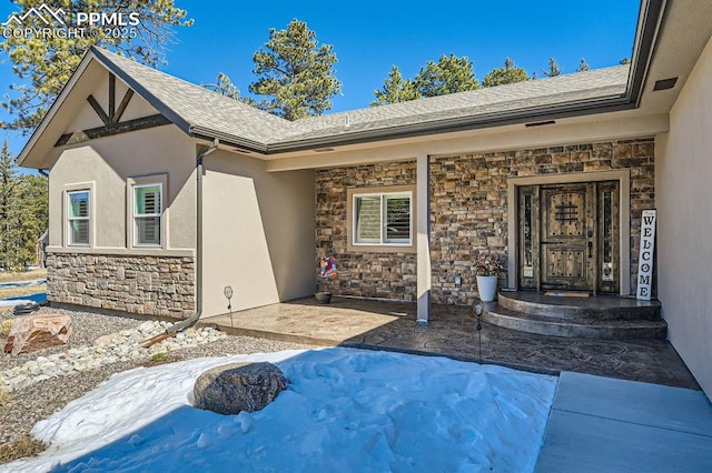 property entrance with a shingled roof, stone siding, and stucco siding