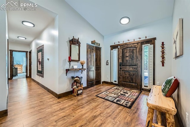 foyer featuring lofted ceiling, wood finished floors, and baseboards