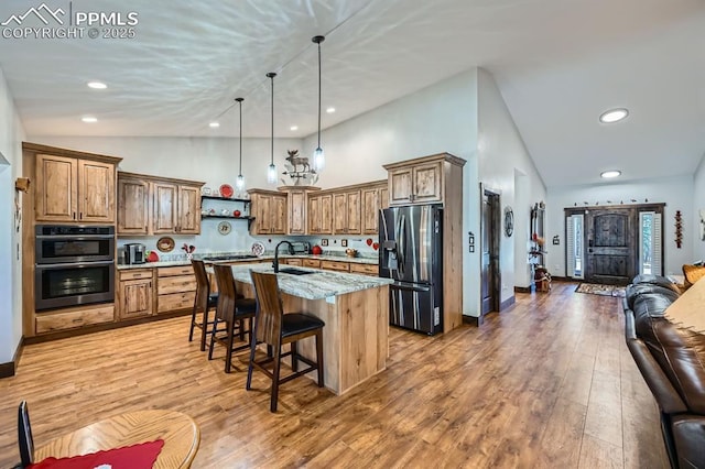 kitchen with brown cabinetry, appliances with stainless steel finishes, a kitchen breakfast bar, open floor plan, and light wood-style floors