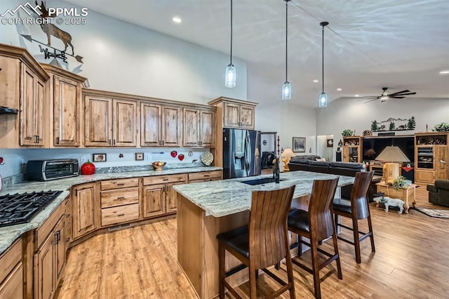 kitchen featuring light stone counters, a toaster, a breakfast bar area, a sink, and stainless steel fridge with ice dispenser