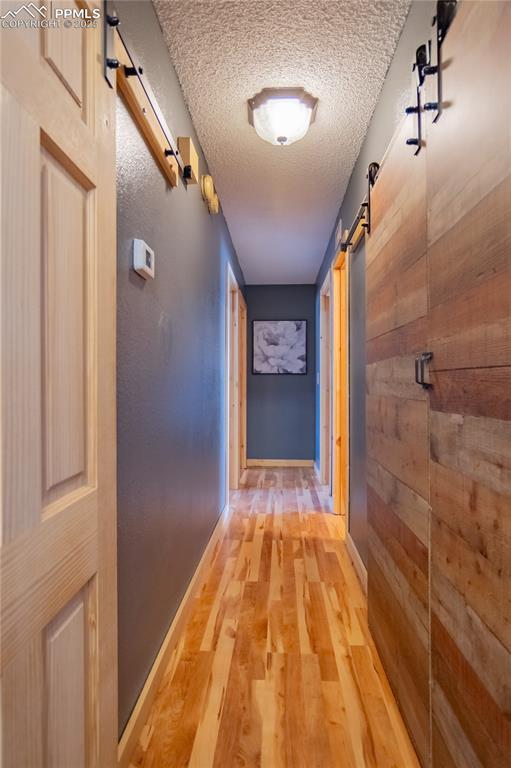 hallway featuring a textured ceiling, wooden walls, a barn door, and light wood-style floors