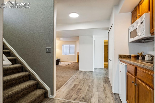 7619 High Gate Dr, Fountain, CO 80817 - interior space featuring brown cabinets, dark countertops, light wood-style flooring, white microwave, and baseboards