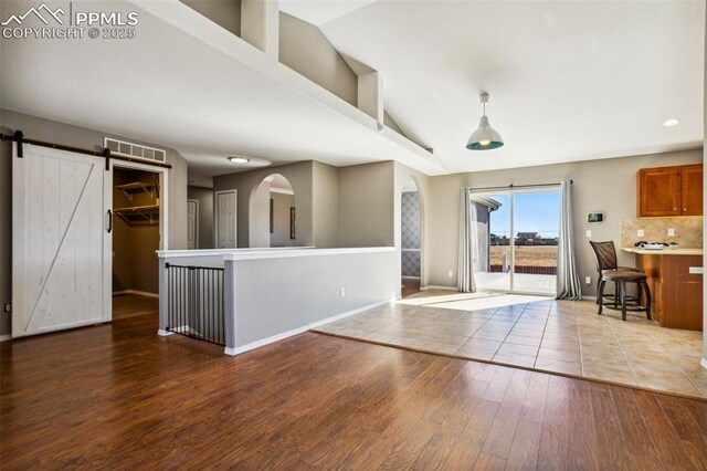 7619 High Gate Dr, Fountain, CO 80817 - kitchen featuring a barn door, wood finished floors, vaulted ceiling, backsplash, and brown cabinets
