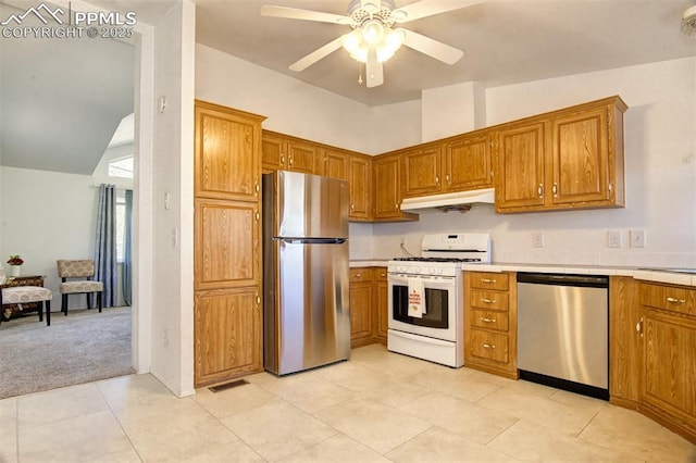 kitchen with stainless steel appliances, a ceiling fan, under cabinet range hood, and brown cabinetry