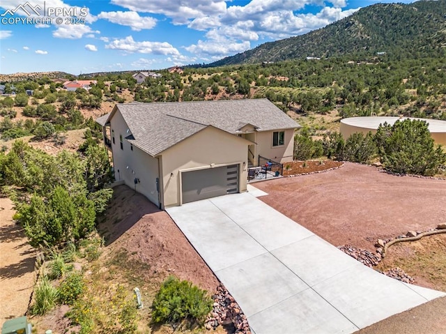 ranch-style home featuring a mountain view, a garage, a shingled roof, driveway, and stucco siding