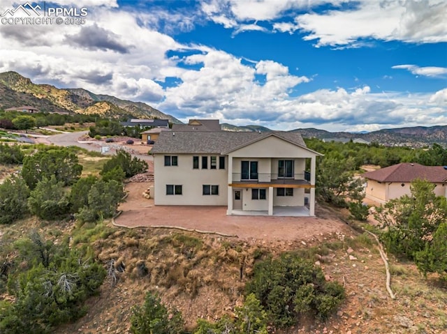 rear view of house with a balcony, a patio area, a mountain view, and stucco siding