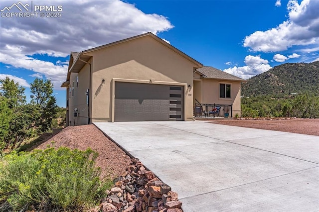 ranch-style home with a garage, driveway, a mountain view, and stucco siding