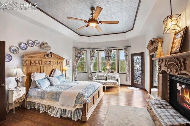 bedroom featuring access to exterior, a raised ceiling, dark wood-type flooring, and a glass covered fireplace