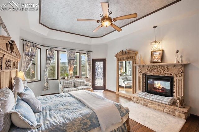 bedroom with baseboards, a raised ceiling, a glass covered fireplace, ornamental molding, and wood finished floors