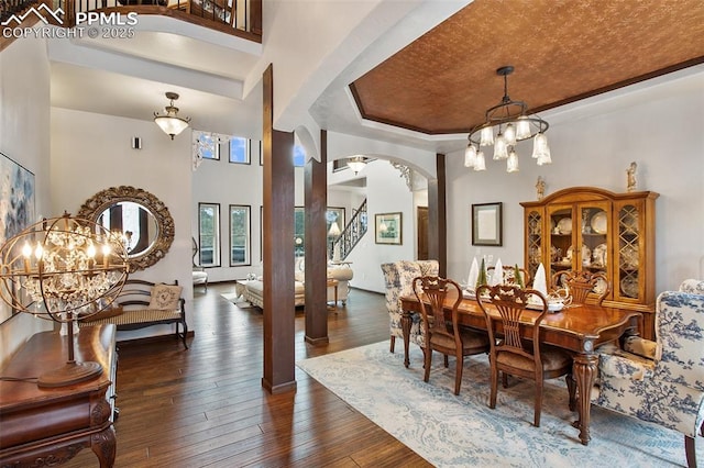 dining space with arched walkways, a chandelier, dark wood-type flooring, a towering ceiling, and a raised ceiling