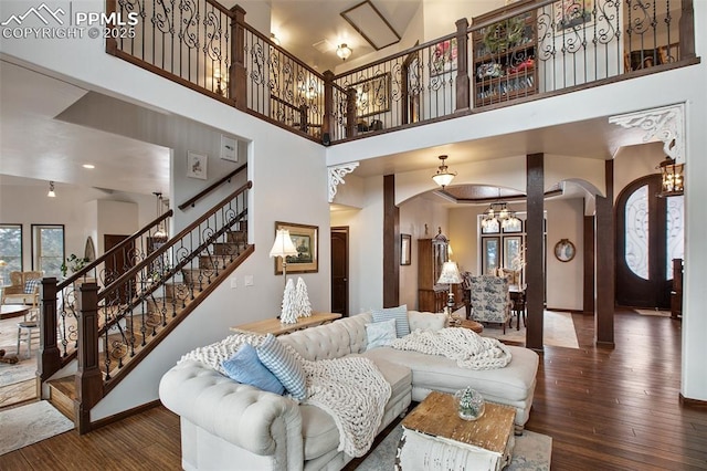 living area featuring stairs, arched walkways, a towering ceiling, and hardwood / wood-style flooring