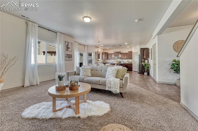 living room with a textured ceiling, a chandelier, wood finished floors, visible vents, and baseboards