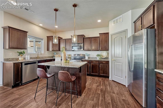 kitchen featuring dark brown cabinetry, visible vents, appliances with stainless steel finishes, a center island, and dark wood finished floors