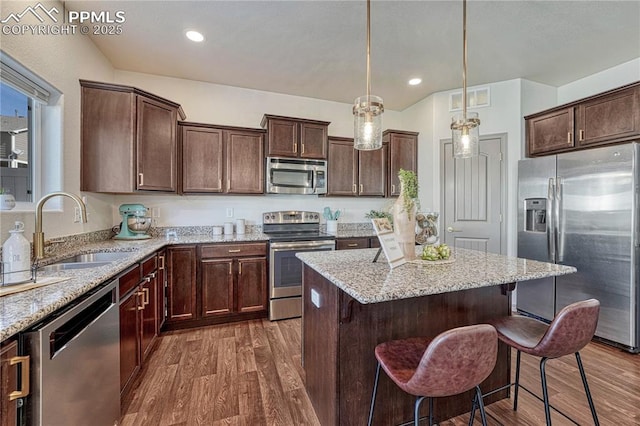 kitchen with a breakfast bar area, stainless steel appliances, a sink, a center island, and dark wood-style floors