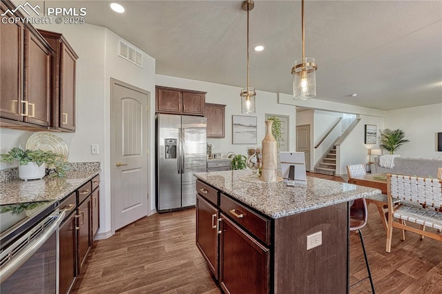 kitchen featuring a breakfast bar area, visible vents, stainless steel appliances, and dark wood finished floors