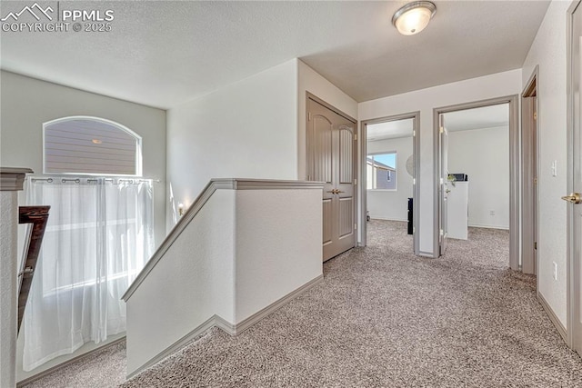 hallway featuring carpet, baseboards, a textured ceiling, and an upstairs landing