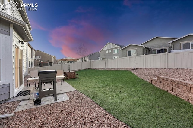 yard at dusk featuring a patio area, a fenced backyard, and a residential view