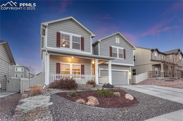 traditional home featuring covered porch, concrete driveway, fence, and a garage