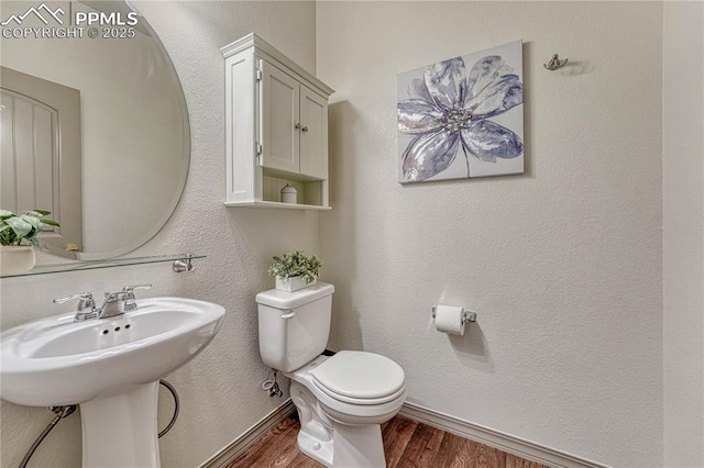 bathroom with toilet, baseboards, wood finished floors, and a textured wall