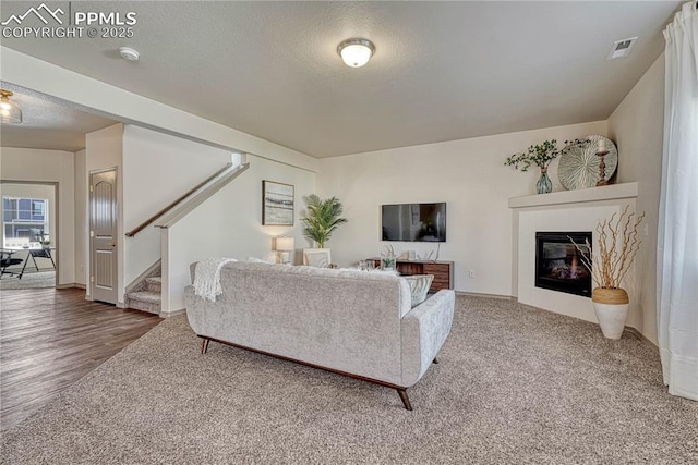 living room featuring visible vents, a textured ceiling, stairway, and a tiled fireplace