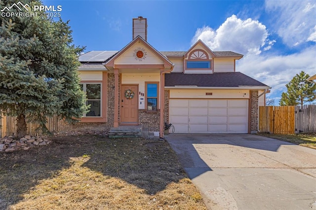 view of front of home with a chimney, concrete driveway, an attached garage, roof mounted solar panels, and fence