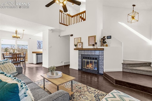 living room featuring baseboards, visible vents, a tile fireplace, wood finished floors, and ceiling fan with notable chandelier