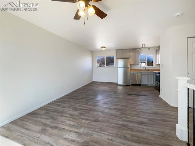 unfurnished living room featuring dark wood-type flooring, a sink, a ceiling fan, and baseboards