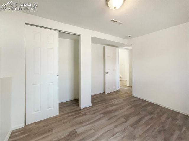 unfurnished bedroom with a closet, wood finished floors, visible vents, and baseboards