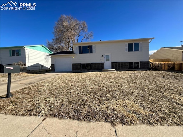 bi-level home with driveway, a garage, fence, and brick siding