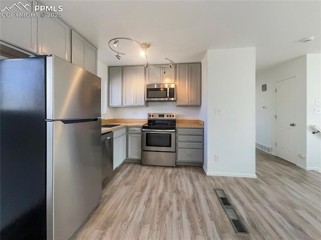 kitchen with stainless steel appliances, gray cabinets, visible vents, and light wood-style flooring