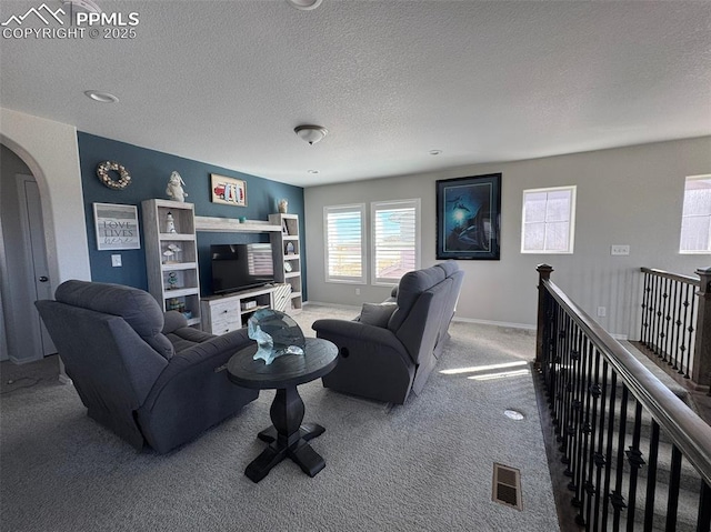 living area with baseboards, visible vents, arched walkways, a textured ceiling, and carpet flooring