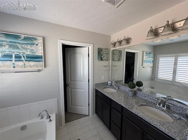 full bathroom with a garden tub, a textured ceiling, visible vents, and a sink