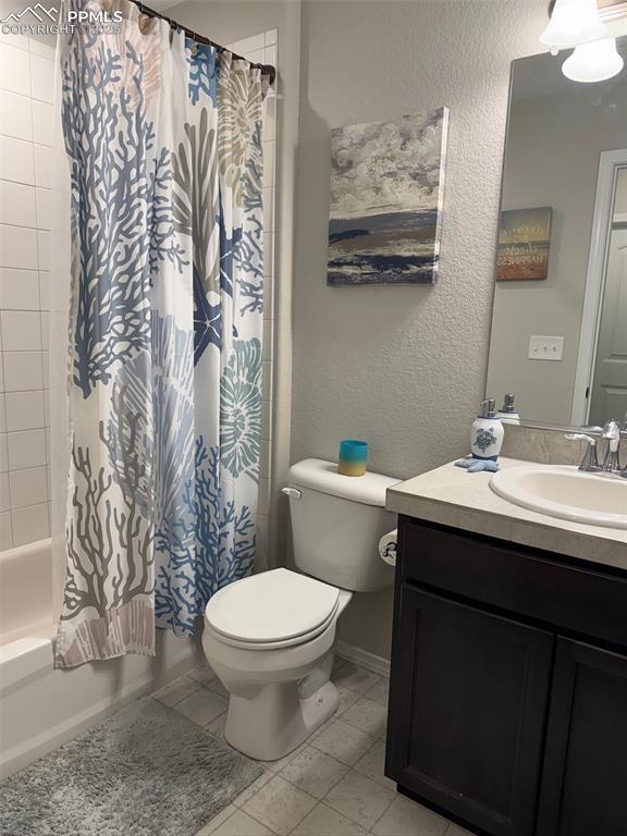 full bath featuring a textured wall, toilet, vanity, baseboards, and shower / bath combo