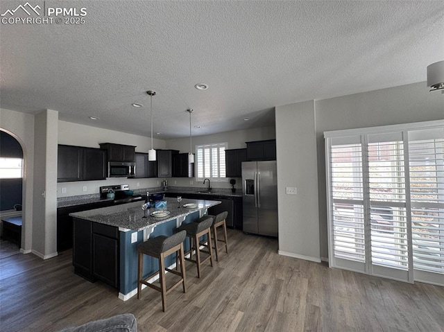 kitchen featuring dark cabinets, wood finished floors, a center island, stainless steel appliances, and a sink