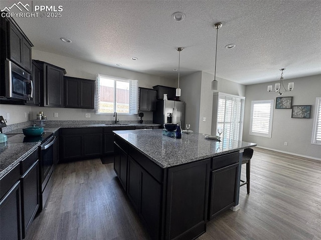 kitchen featuring appliances with stainless steel finishes, a sink, light wood-style floors, and dark cabinets