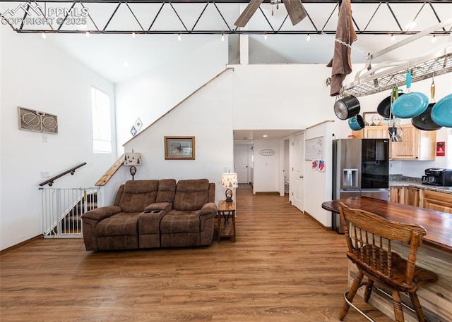 living area with baseboards, a high ceiling, a ceiling fan, and light wood-style floors