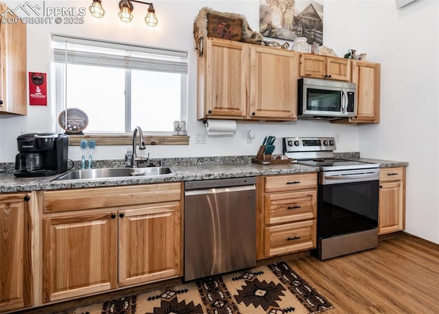 kitchen with stainless steel appliances, dark countertops, a sink, and wood finished floors