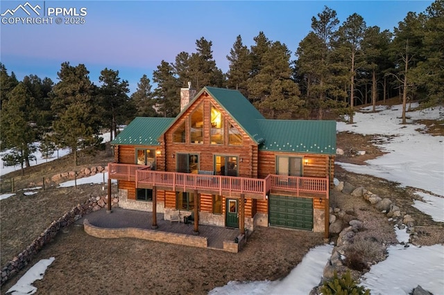 view of front facade with a patio, a chimney, stone siding, a deck, and metal roof