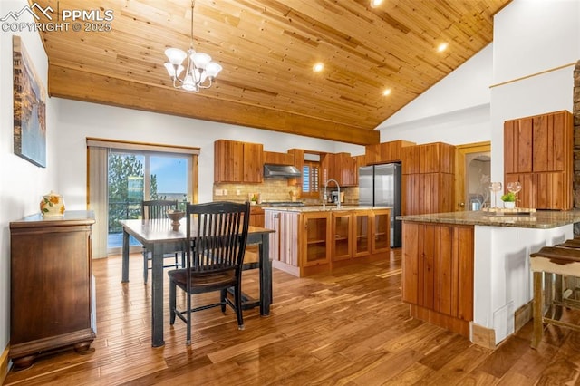 kitchen with wooden ceiling, under cabinet range hood, brown cabinetry, and freestanding refrigerator